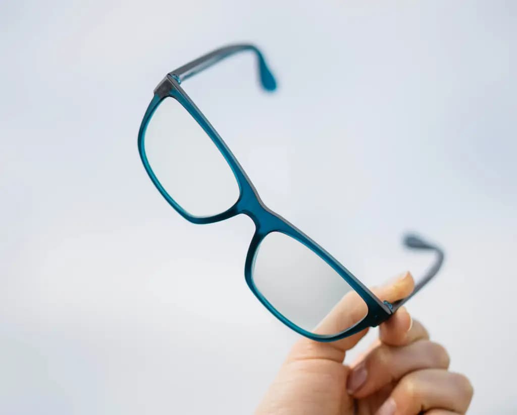 Close-up of contemporary Dresden Vision blue eyeglass frames held against a minimal white background