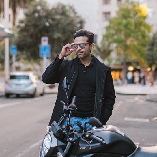 Stylish man in mirrored sunglasses leaning near bike on city street, repping Dresden Vision Canada eyewear.