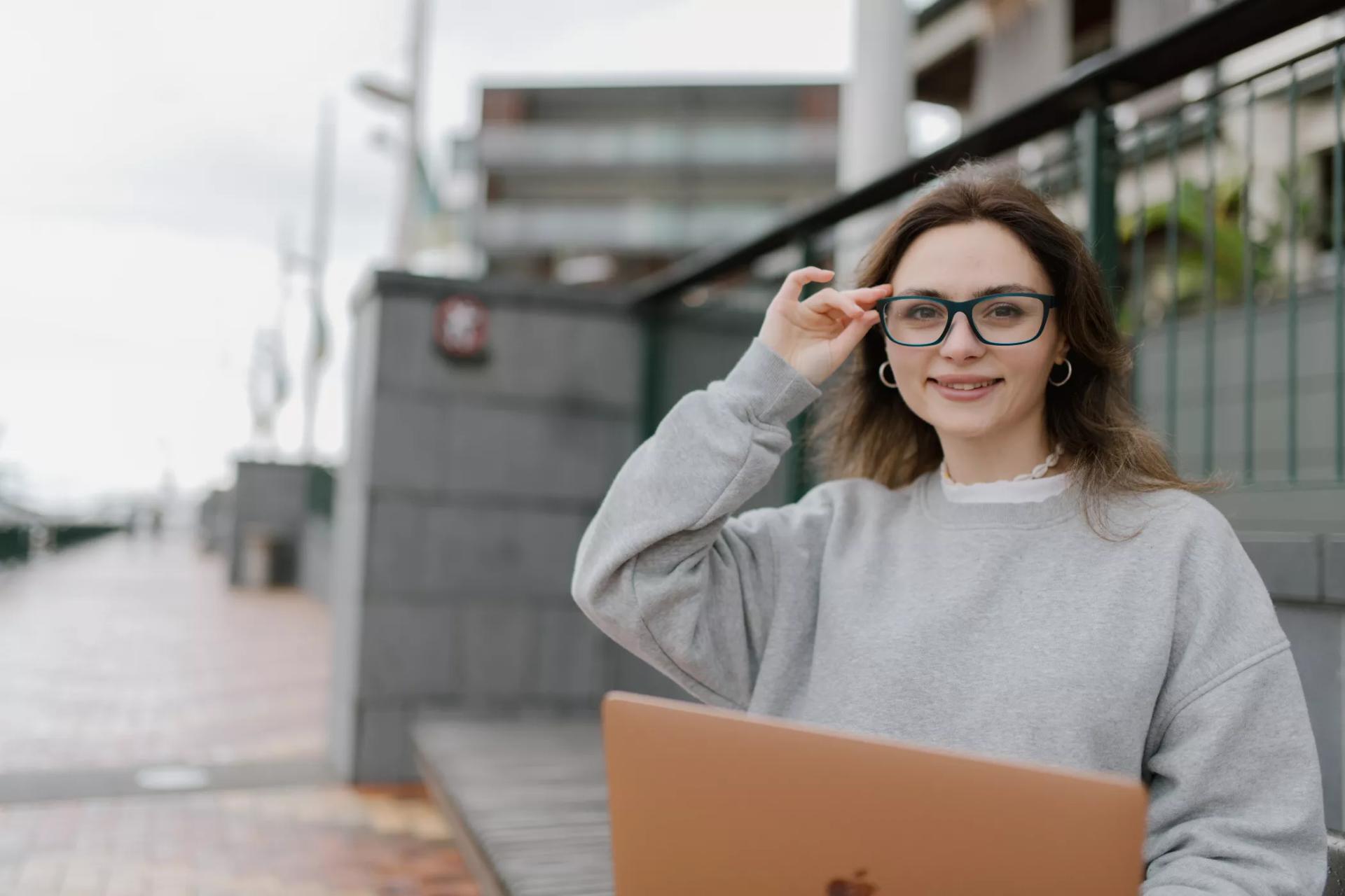 Woman with long brown hair wearing blue-framed Dresden Vision glasses smiles while adjusting her eyewear. She