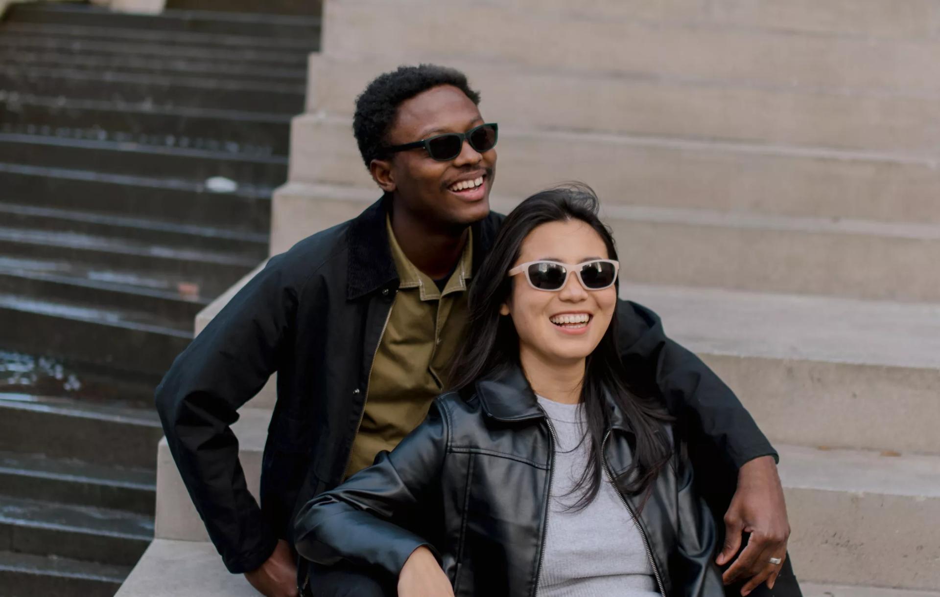 Two persons relaxing on outdoor steps, wearing Dresden Vision prescription sunglasses in New Zealand. Their comfort and satisfaction highlight the quality and fit of the eyewear.