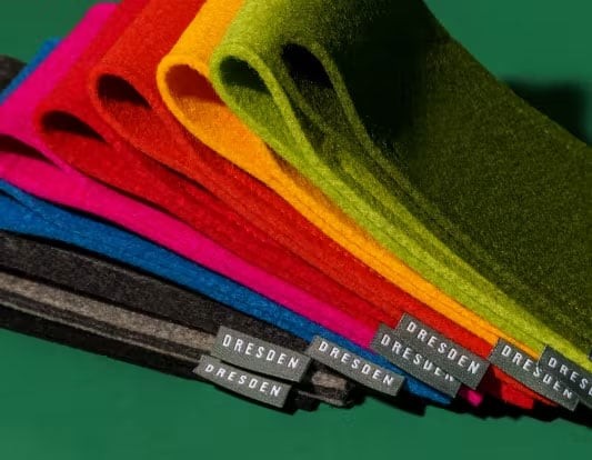 A stack of wool in various colors used for making felt cases, featuring a 'DRESDEN' tag. The image showcases the material variations used for Dresden Vision’s accessories.