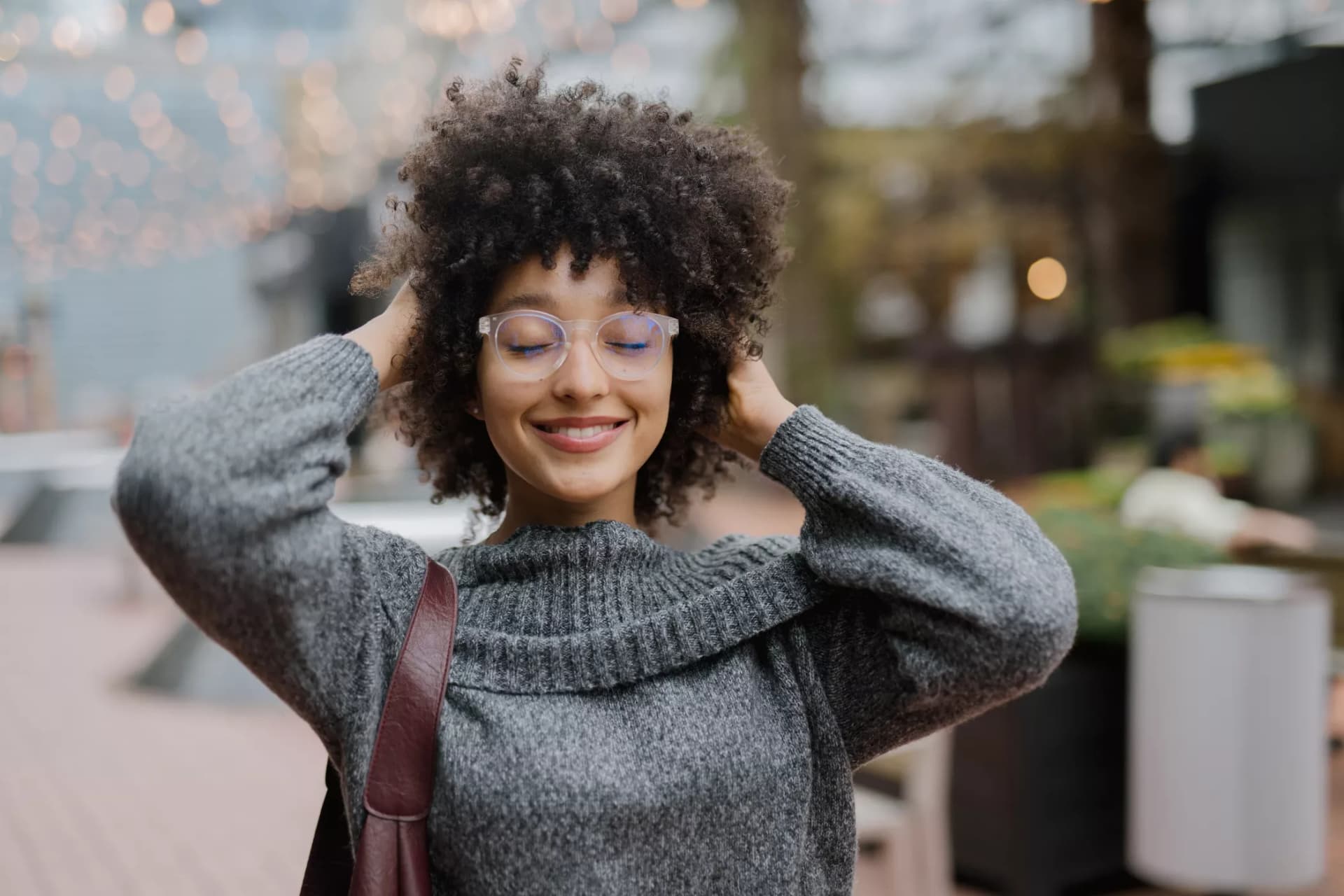 Carefree woman with curly hair and bifocal lenses in New Zealand, basking in natural light while dressed in a warm knit.